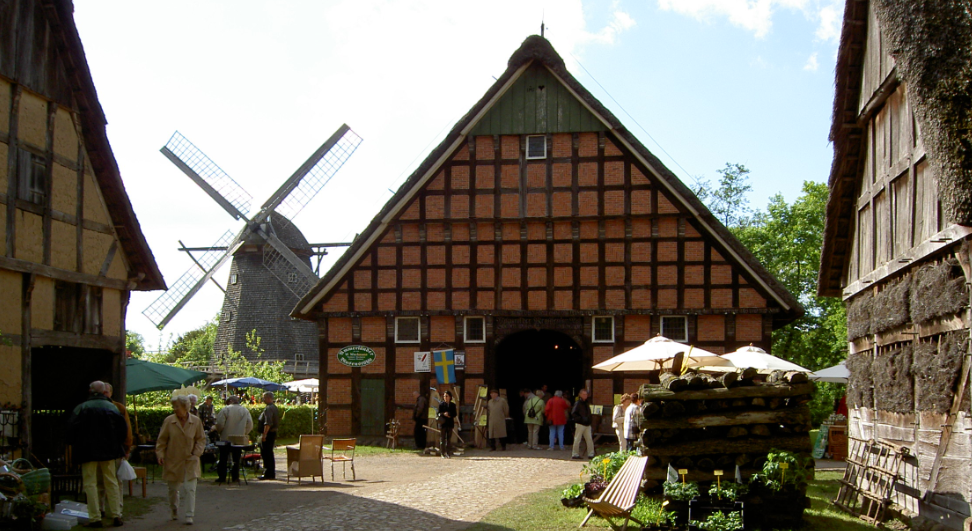 Scheune mit grossem Tor, Menschen stehen davor und im Hintergrund steht eine Mühle mit Flügeln